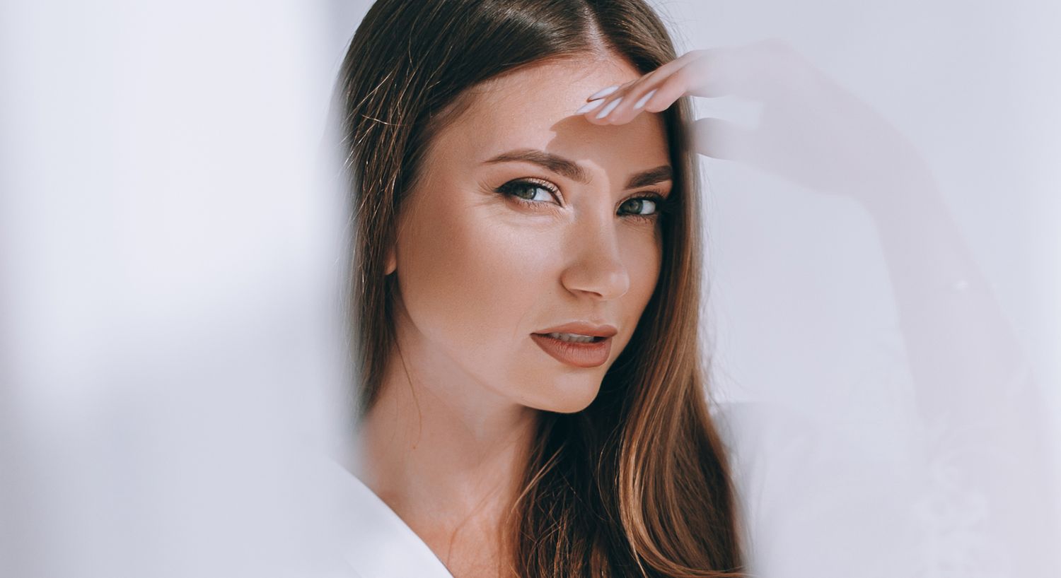 Woman with long hair posing near window curtain.